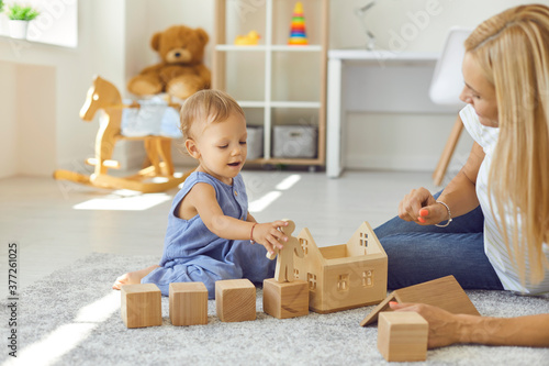 Cheerful young babysitter and little kid playing with wooden blocks in cozy room photo