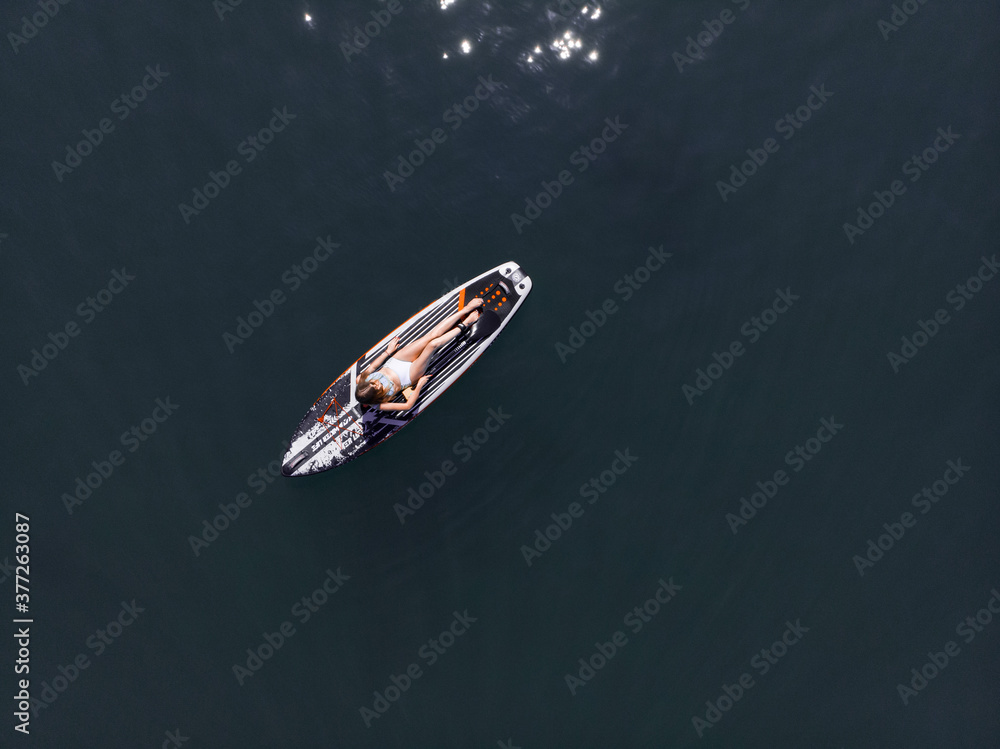 Naklejka premium Attractive Woman on Stand Up Paddle Board, Woman paddling on sup board and enjoying turquoise transparent water. Tropical travel, wanderlust and water activity concept. Sunset and relax