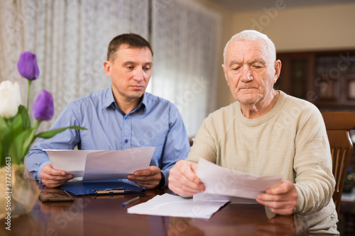 Mature man and realtor fills in documents for purchase of apartment in living room