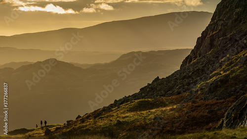 A Group of walkers are silhouetted against a hazy yellow backdrop of Lakeland Fells photo