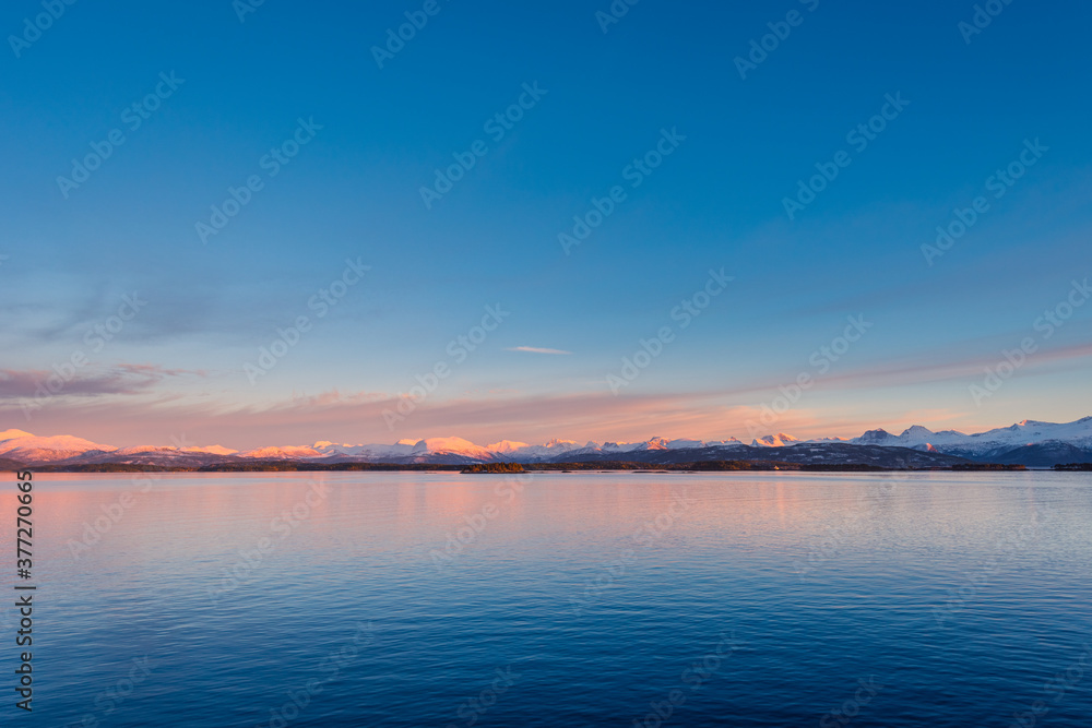 Panoramic vista of the coast of Norway with snow covered mountains in beautiful soft evening light
