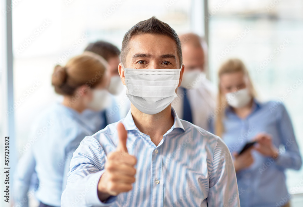 business, people and pandemic concept - middle aged businessman wearing face protective medical mask for protection from virus disease showing thumbs up at office