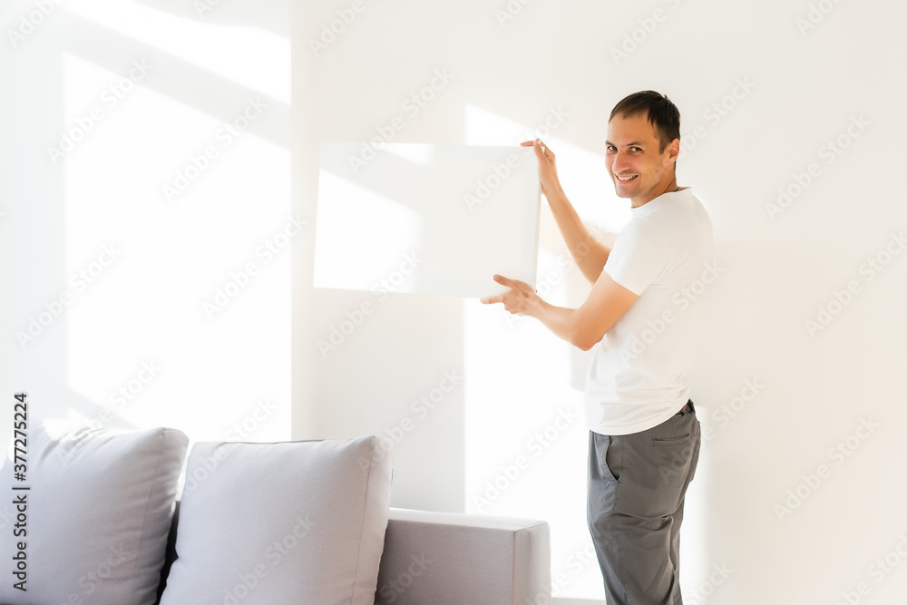 Young man in white t-shirt is holding blank empty canvas. Guy student is smiling. Template for advertising, greeting, invitation. Emotional portrait Young man in white t-shirt is holding blank empty canvas. Guy student is smiling. Template for advertising, greeting, invitation. Emotional portrait