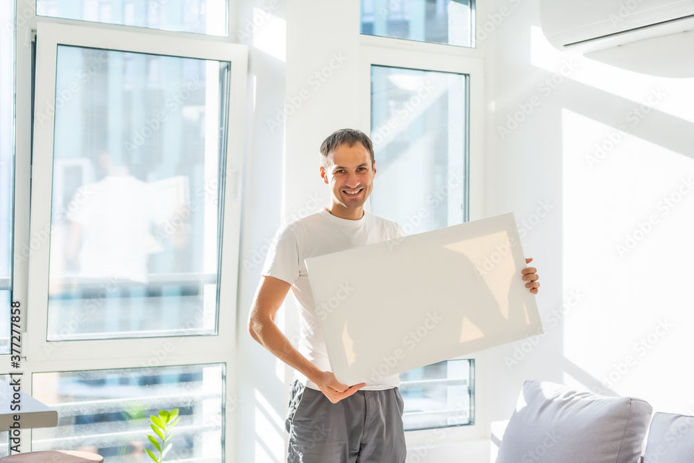Young man in white t-shirt is holding blank empty canvas. Guy student is smiling. Template for advertising, greeting, invitation. Emotional portrait