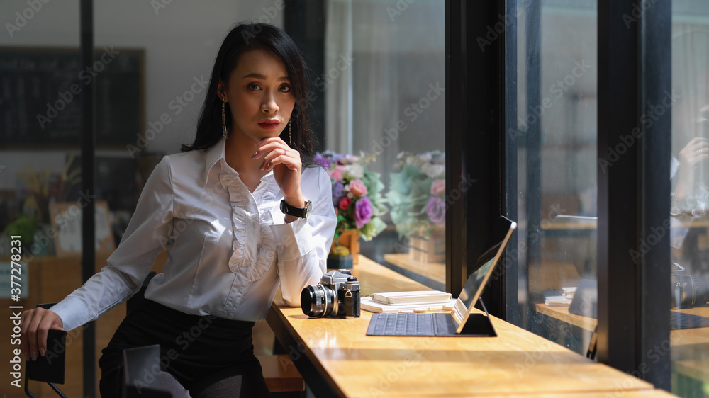 Attractive female freelancer sitting at wooden bar with camera and digital tablet in cafe Attractive female freelancer sitting at wooden bar with camera and digital tablet in cafe