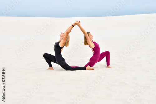 Two beautiful young women performing yoga pose together on the sand © sonsedskaya