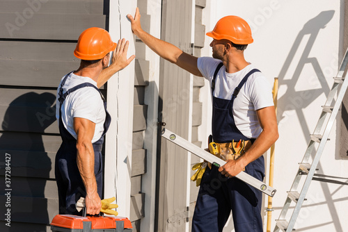 Builders in uniform and hardhats touching facade of building outdoors