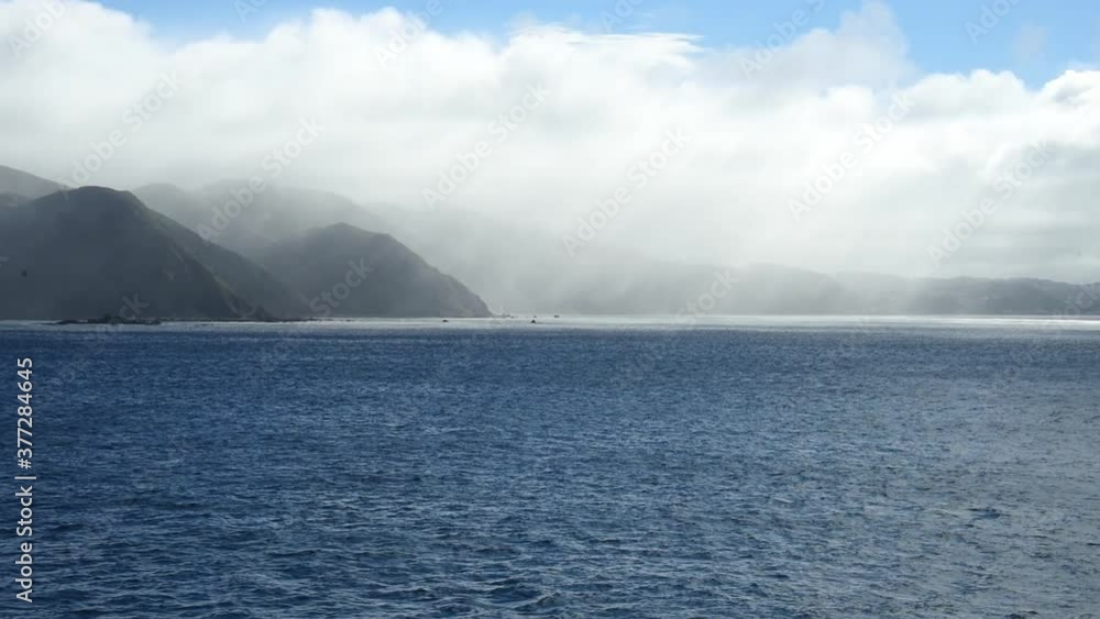 Dramatic clouds above the southern end of New Zealand North Island. Rain in the distance of the cliffs at the coast Dramatic clouds above the southern end of New Zealand North Island. Rain in the distance of the cliffs at the coast
