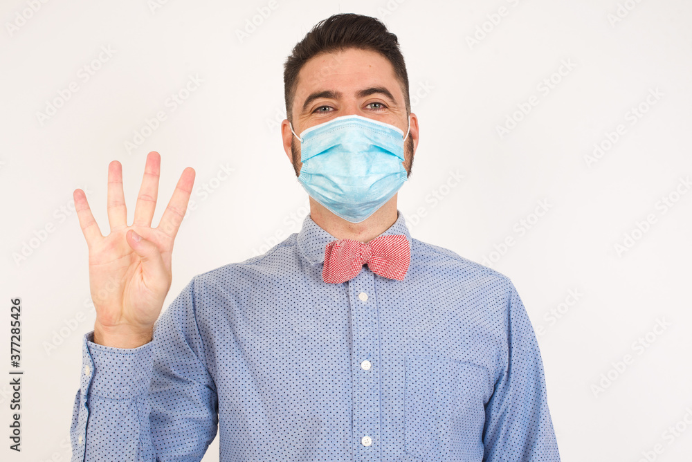 Young man standing against gray wall showing and pointing up with fingers number four while smiling confident and happy. Young man standing against gray wall showing and pointing up with fingers number four while smiling confident and happy.