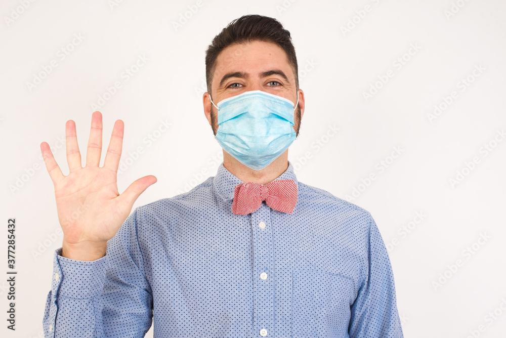 Young man standing against gray wall showing and pointing up with fingers number five while smiling confident and happy. Young man standing against gray wall showing and pointing up with fingers number five while smiling confident and happy.