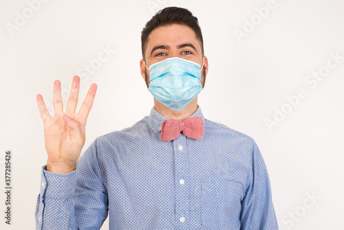 Young man standing against gray wall showing and pointing up with fingers number four while smiling confident and happy.