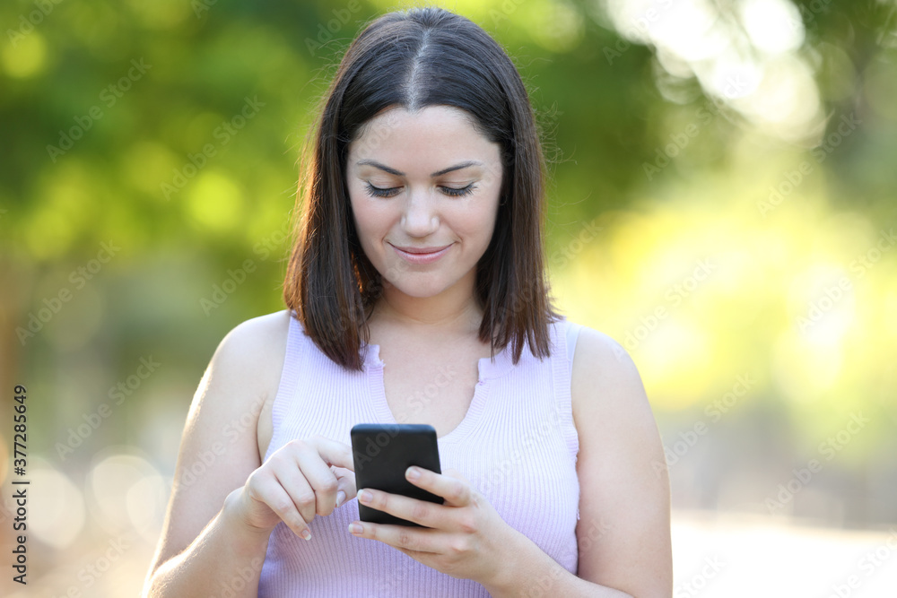 Serious woman using phone walking in a park