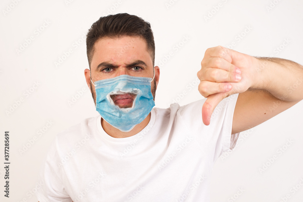 Discontent European man shows disapproval sign, keeps thumb down, expresses dislike, frowns face in discontent, dressed in white shirt, isolated over gray background. Body language concept. Discontent European man shows disapproval sign, keeps thumb down, expresses dislike, frowns face in discontent, dressed in white shirt, isolated over gray background. Body language concept.