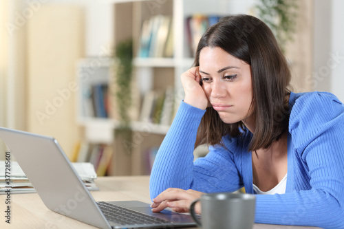 Foto Bored woman checking laptop on a desk at home
