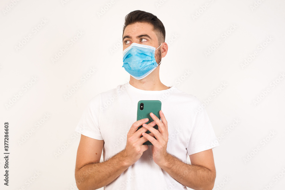 Portrait of handsome young man with dreamy look, thinking while holding smartphone, isolated over yellow background. Tries to write up a message for her father, explaining why he took car