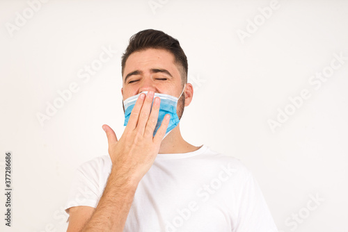 Shot of sleepy attractive caucasian man yawning with messy brown hair, feeling tired after night without sleep, yawning, covering opened mouth with palm.