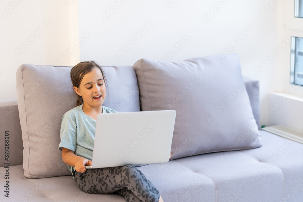 Little girl of school age is studying at home. A girl watches a video lesson on a laptop monitor and writes tasks in a notebook. Little girl of school age is studying at home. A girl watches a video lesson on a laptop monitor and writes tasks in a notebook.