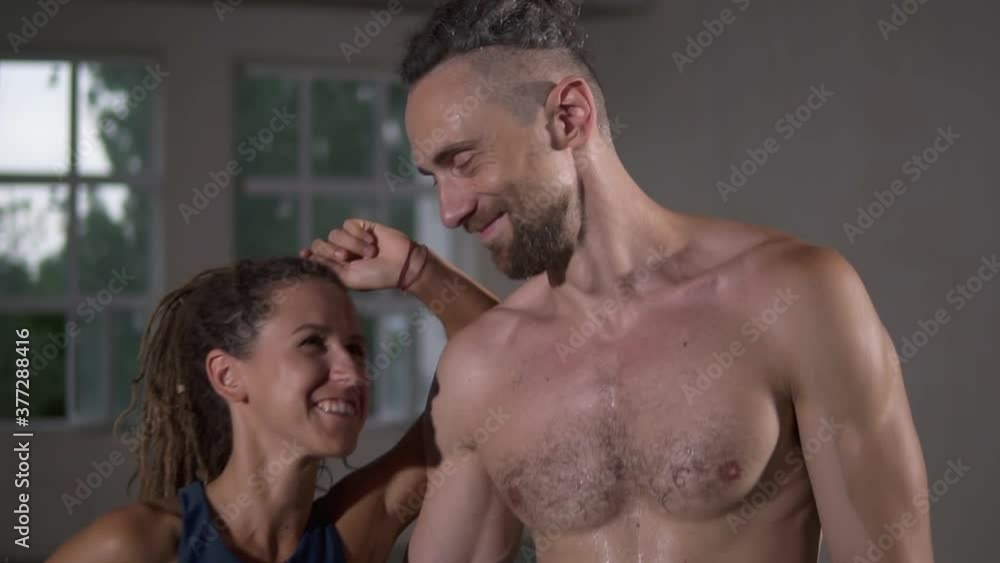 Happy couple with dreadlocks after successful training in sports club together. Sport woman looking on her shirtless handsome partner or trainer, smiling to each other embracing Happy couple with dreadlocks after successful training in sports club together. Sport woman looking on her shirtless handsome partner or trainer, smiling to each other embracing