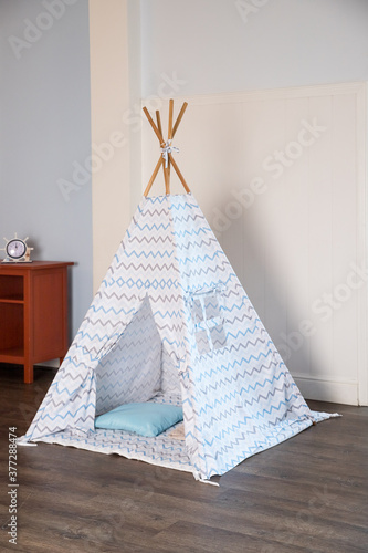 Children's hut with toys in the room. Interior of the children's room with tent-hut for children's games in boho style, bright interior of the children's room with a wigwam.Scandinavian style © Yulia