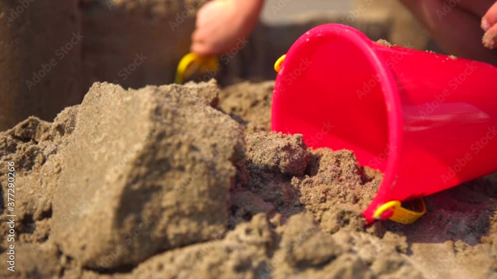 Red bucket on sandy beach with child building a sand castle in the background. (slow motion) Red bucket on sandy beach with child building a sand castle in the background. (slow motion)