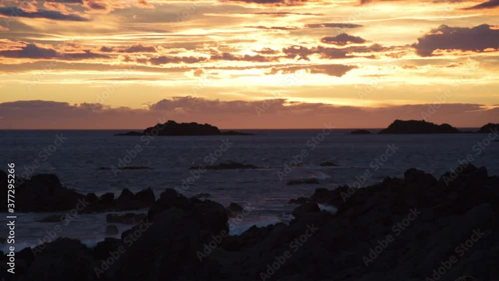 warm sunset with dramatic clouds above the sea with waves breaking into dark rocks warm sunset with dramatic clouds above the sea with waves breaking into dark rocks