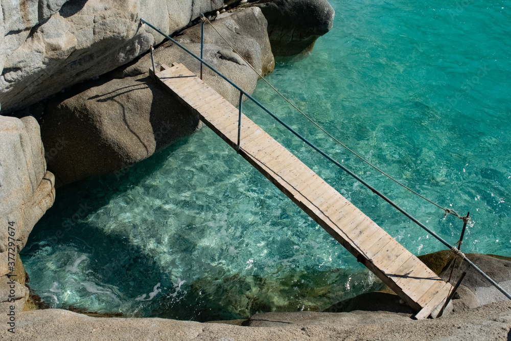 Wooden bridge over crystal water on the Seychelles beach in Ikaria