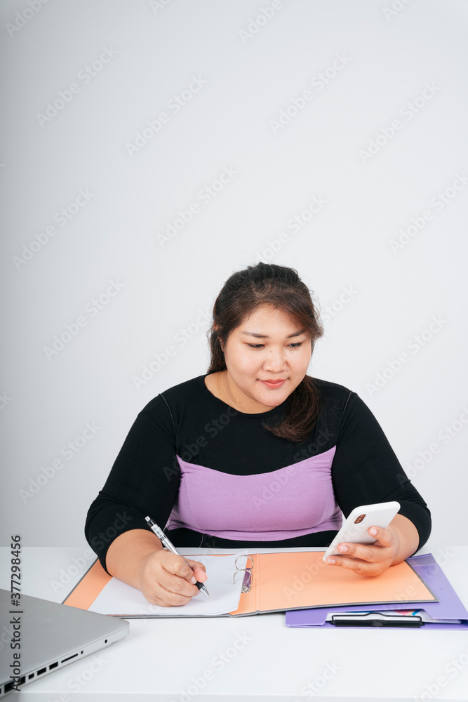 Asian chubby business woman working at desk holding smartphone. Asian chubby business woman working at desk holding smartphone.