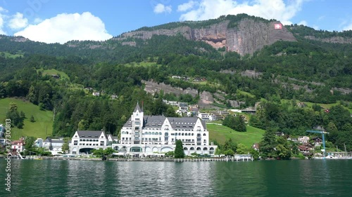 Panorama of Lake Lucerne shoreline with beautiful buildings and mountains with Swiss flag taken from a moving cruise boat in Vitznau Switzerland photo