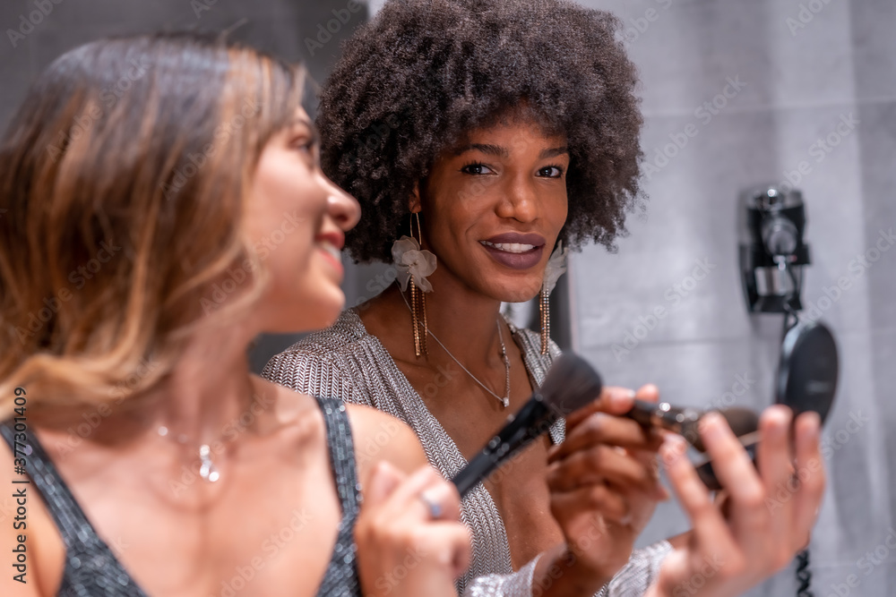 A young black girl with afro hair and a blonde Caucasian girl putting on makeup before the party with a smile. Exclusive party, vip party, gray and blue evening dress A young black girl with afro hair and a blonde Caucasian girl putting on makeup before the party with a smile. Exclusive party, vip party, gray and blue evening dress