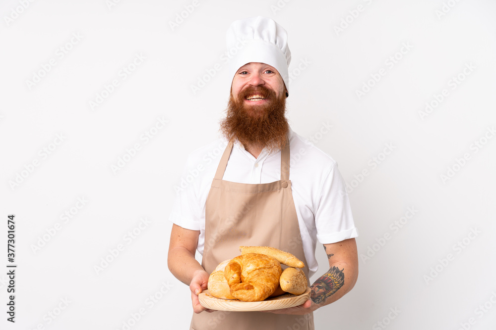 Redhead man in chef uniform. Male baker holding a table with several breads smiling a lot