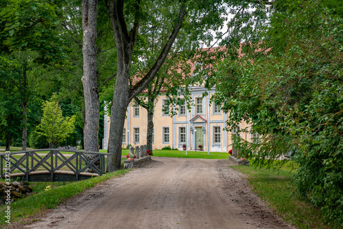 Rural road leads to the old manor in Eclectic style. Gravel path street with green trees in summer.