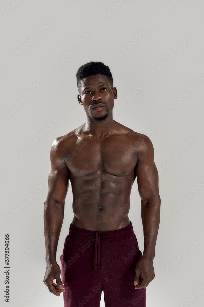 Strength. Muscular african american man looking at camera, showing his naked torso while posing shirtless isolated over grey background. Sports, workout, bodybuilding concept Strength. Muscular african american man looking at camera, showing his naked torso while posing shirtless isolated over grey background. Sports, workout, bodybuilding concept