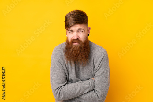 Redhead man with long beard over isolated yellow background freezing