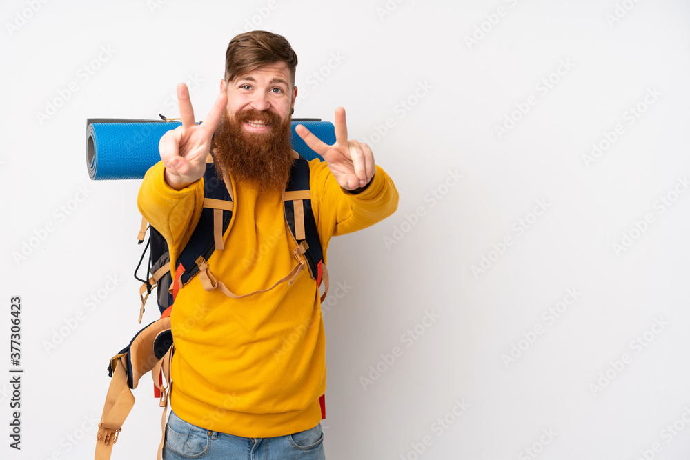 Young mountaineer man with a big backpack over isolated white background smiling and showing victory sign Young mountaineer man with a big backpack over isolated white background smiling and showing victory sign