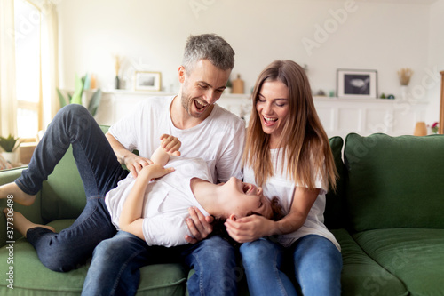 Laughing family tickling cute small child son playing together on sofa in living room. Concept of healthy happy family, weekend activities with children indoor. Happy parenting