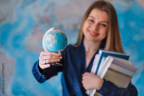 Smiling young student girl hold in hands globe and books