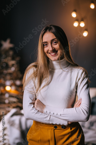 Beautiful young woman in a white sweater against the background of Christmas decorations and lights. Close-up. © Ivan