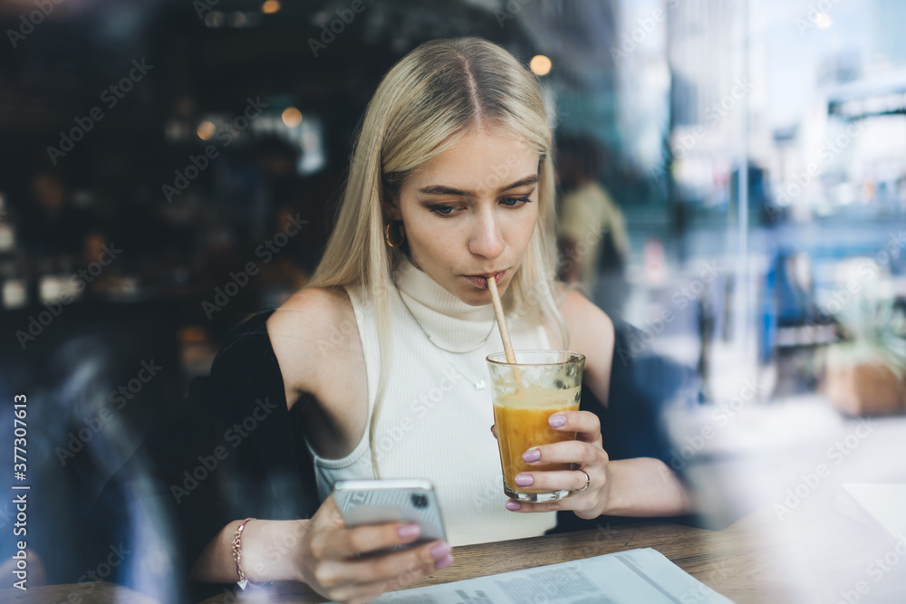 Concentrated woman drinking juice and using smartphone