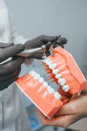 The hands of a dentist doctor hold a model of human's jaw and remove the tartar.