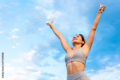 Fitness session with a young Caucasian blonde, very cheerful doing exercises, with the sky in the background, symbol of vistoria, gray sport suit, fit girl, healthy life, exercise in the field