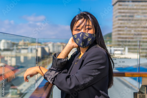 Young Chinese brunette tourist with face mask visiting the city in the new normal on vacation. Asian girl summer lifestyle, social distance, covid-19, coronavirus