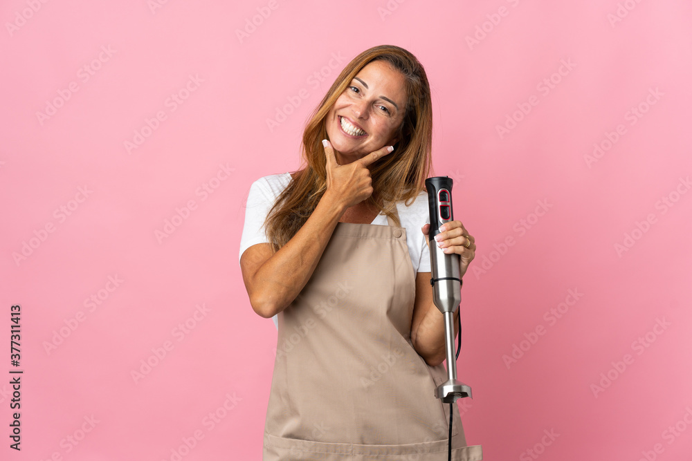 Middle age woman using hand blender isolated on pink background happy and smiling Middle age woman using hand blender isolated on pink background happy and smiling