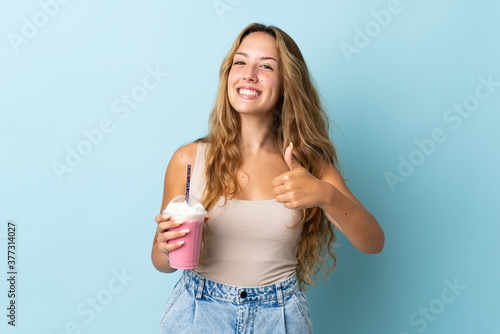 Young woman with strawberry milkshake isolated on blue background giving a thumbs up gesture