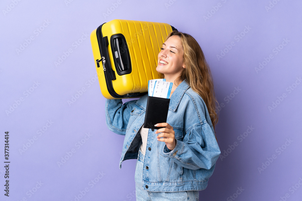 Young blonde woman isolated on purple background in vacation with suitcase and passport Young blonde woman isolated on purple background in vacation with suitcase and passport