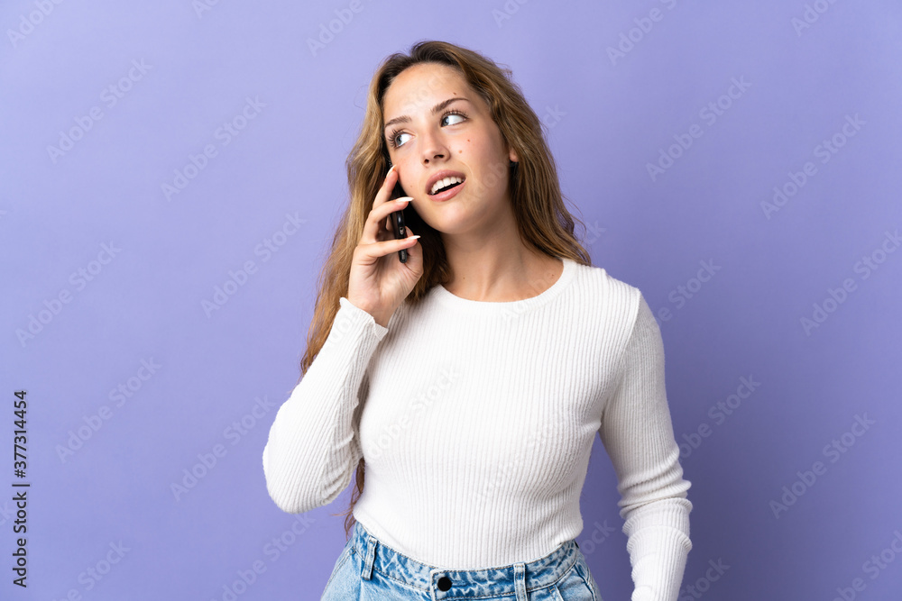 Young blonde woman isolated on purple background keeping a conversation with the mobile phone with someone Young blonde woman isolated on purple background keeping a conversation with the mobile phone with someone