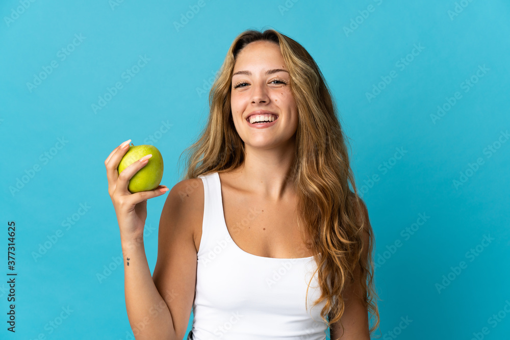 Young blonde woman isolated on blue background with an apple and happy Young blonde woman isolated on blue background with an apple and happy