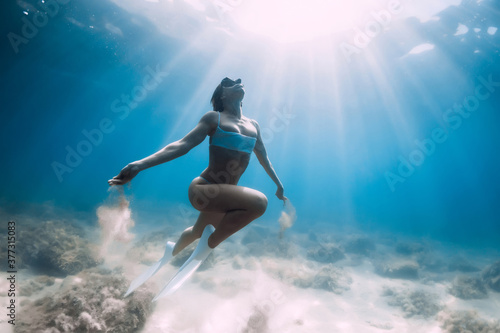 Freediver woman glides and posing over sandy sea with white freediving fins.