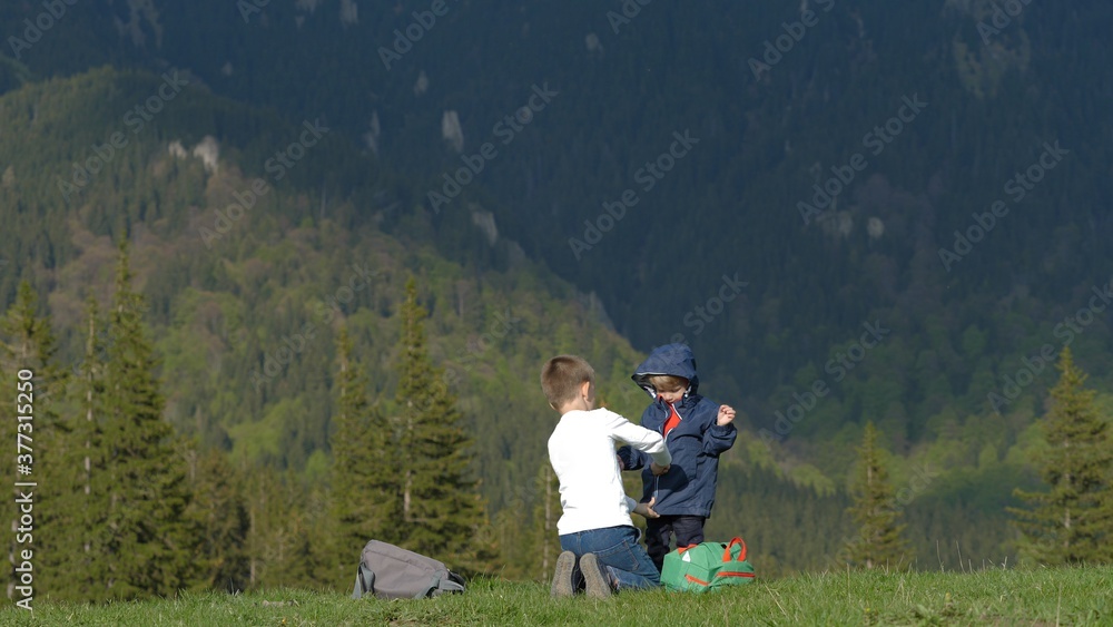 Child help little brother to dress, prepare for travel in mountains, real love