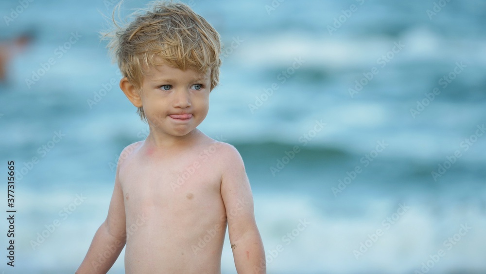 Portrait of little child with blue eyes, wind waves blond hair, funny boy at sea, fluttering, slow motion