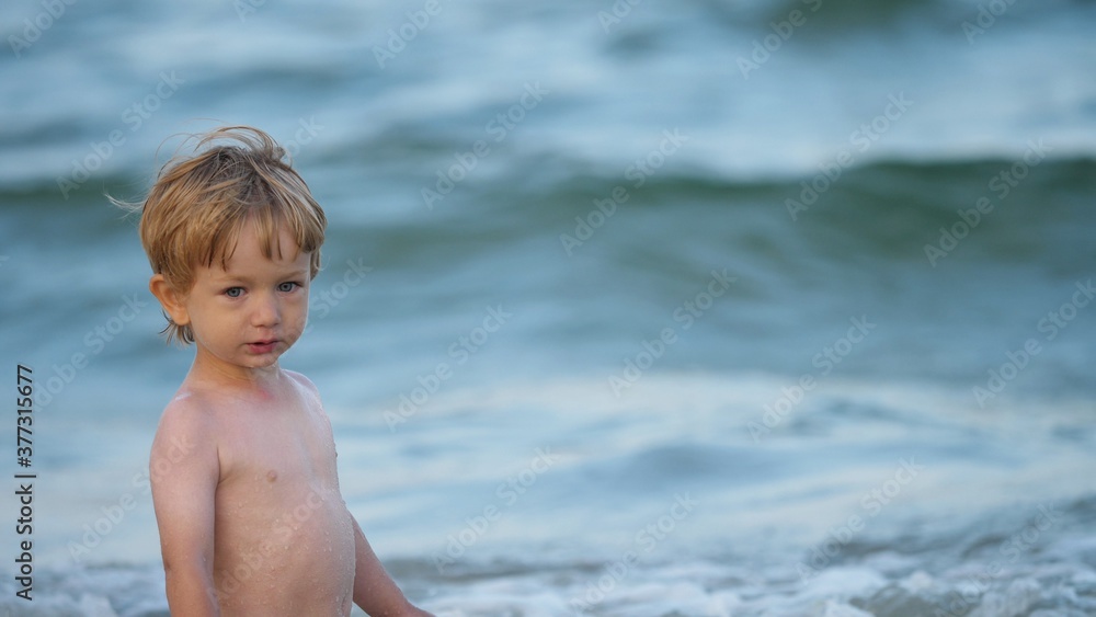 Funny child with blue eyes and blond hair, sea waving background Funny child with blue eyes and blond hair, sea waving background
